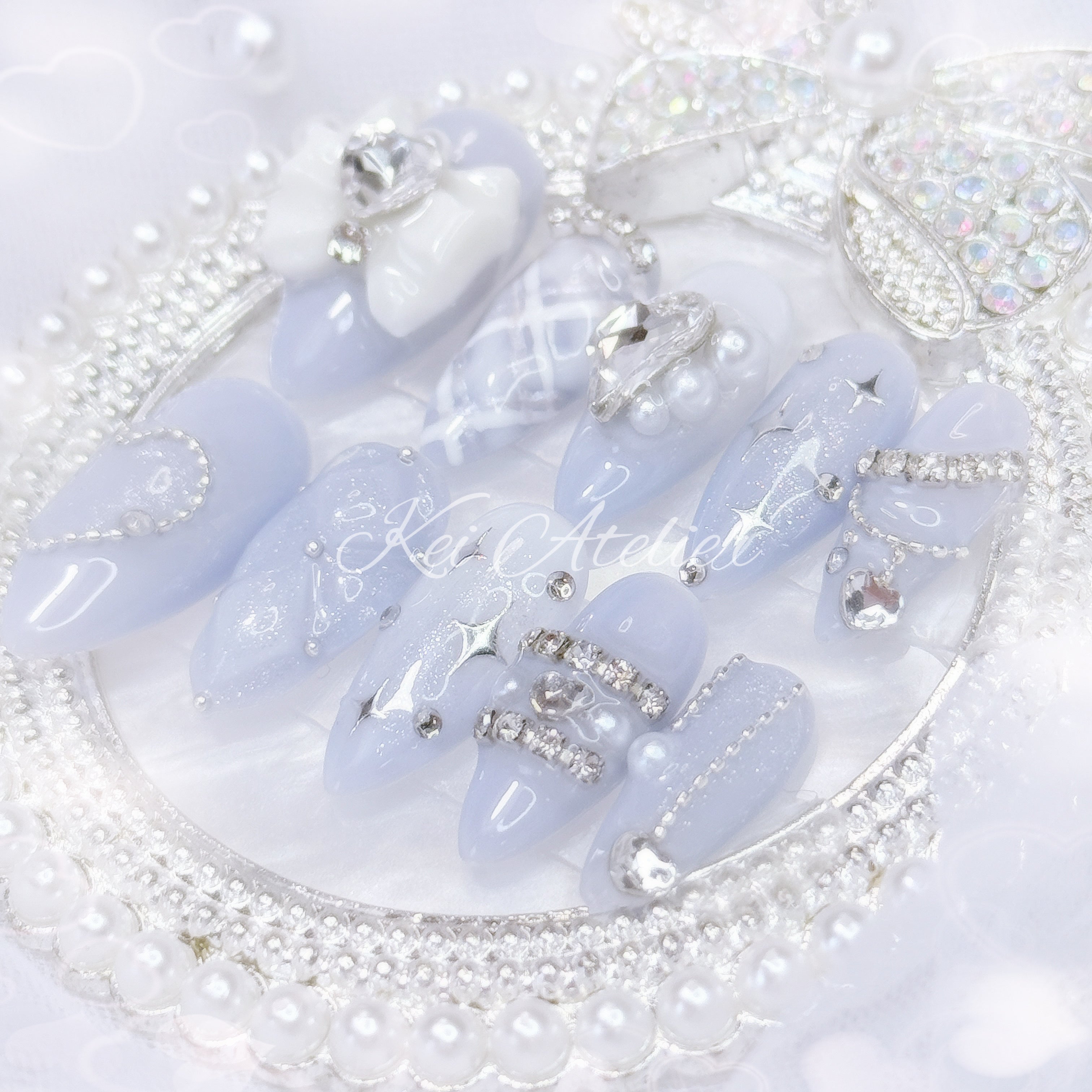 Kawaii Japanese ryousangata jirai style handmade press-on nail set featuring milky blue and white gels, glitter, shimmer, 3d cushion design, silver startlight stickers, pearls, rhinestones, ribbon and bow charms, inspired by moonlight