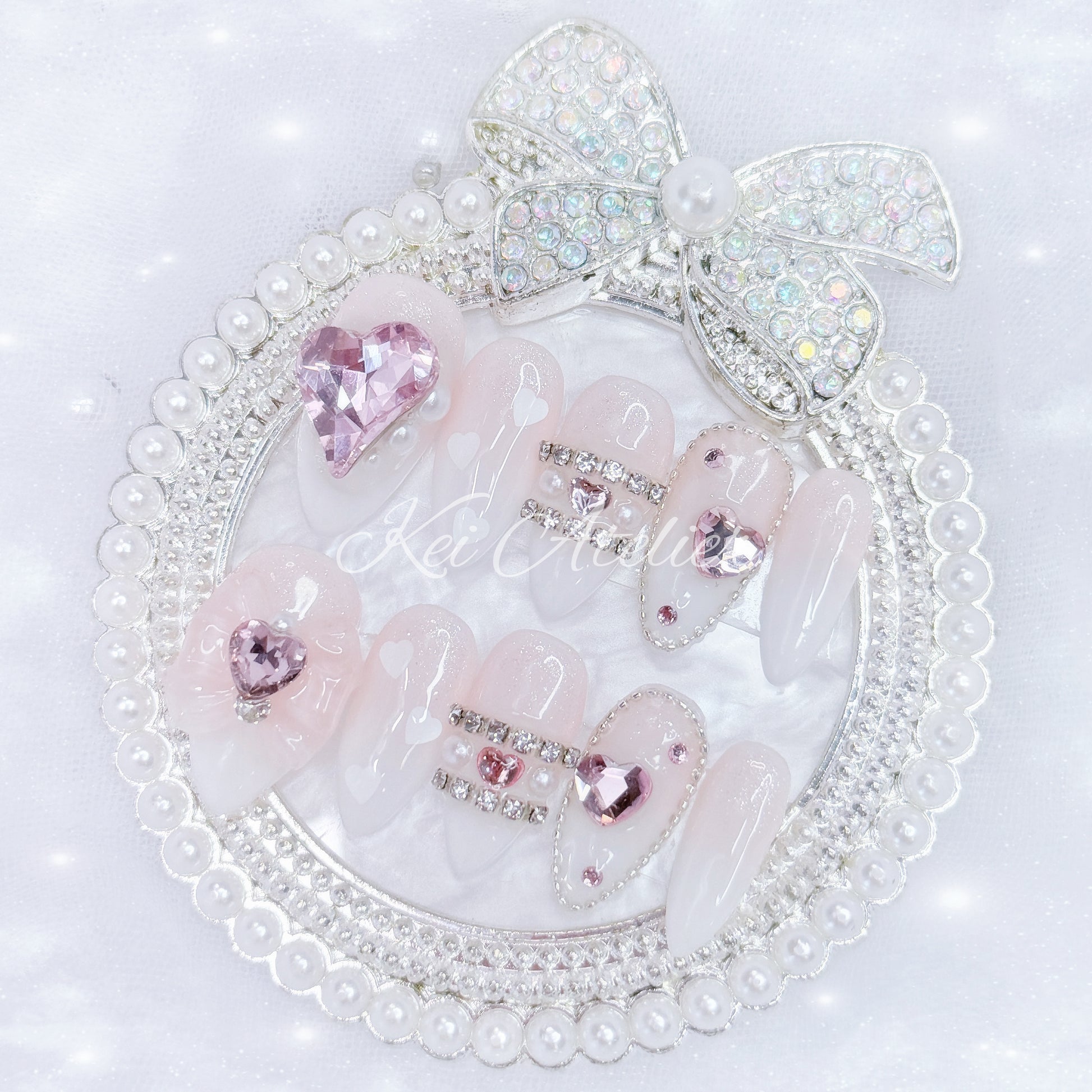 Kawaii Japanese ryousangata jirai style handmade press-on nail set featuring pink and white ombre, sugary sparkles, and bejeweled in pink heart crystals, a ribbon, and white hearts