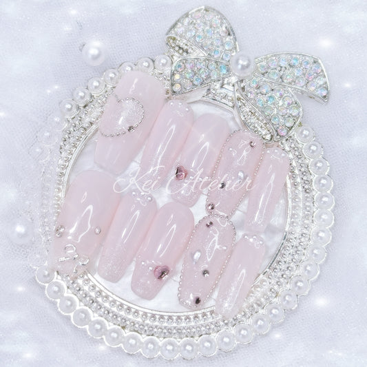 Kawaii Japanese ryousangata jirai style handmade press-on nail set featuring baby pink gel, sparkly shimmery glitter, bejeweled with tiny pink rhinestones and pearls, heart crystals and a silver bow