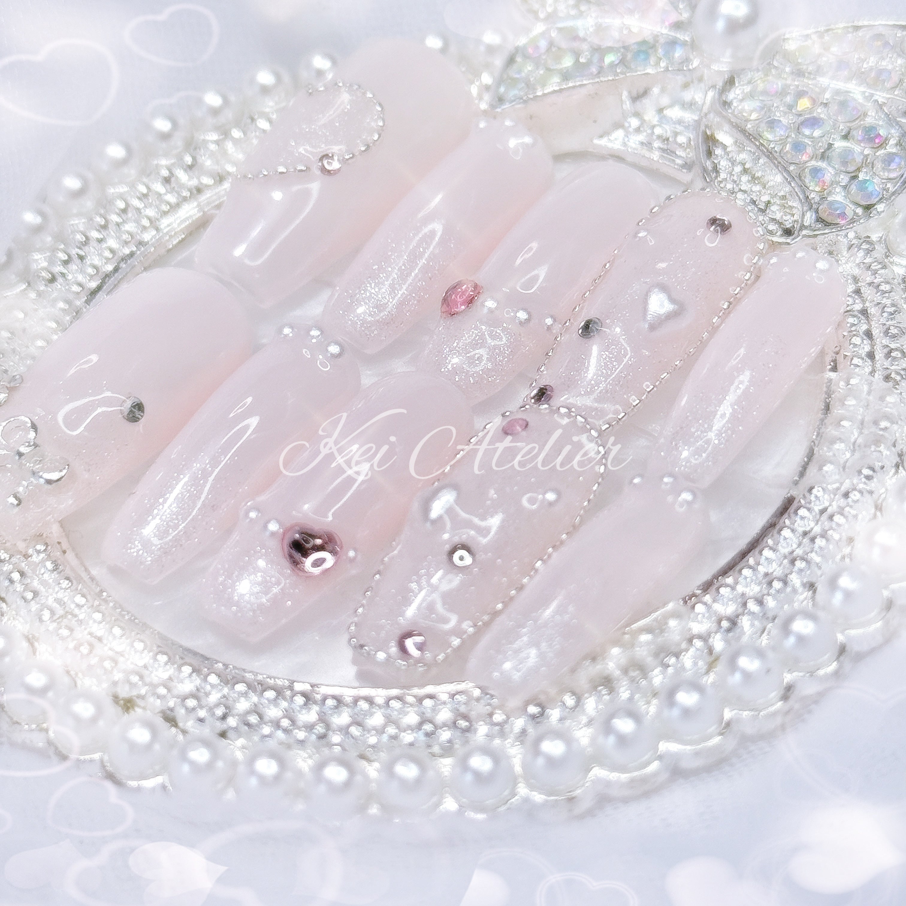Kawaii Japanese ryousangata jirai style handmade press-on nail set featuring baby pink gel, sparkly shimmery glitter, bejeweled with tiny pink rhinestones and pearls, heart crystals and a silver bow