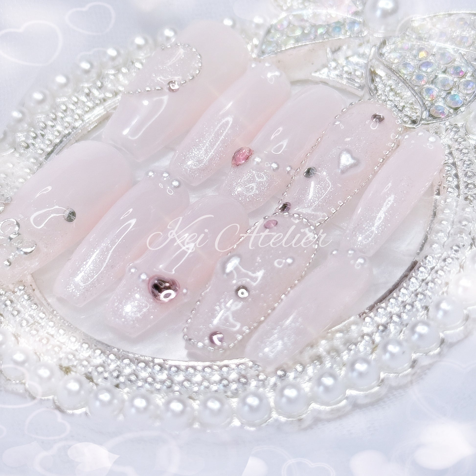 Kawaii Japanese ryousangata jirai style handmade press-on nail set featuring baby pink gel, sparkly shimmery glitter, bejeweled with tiny pink rhinestones and pearls, heart crystals and a silver bow